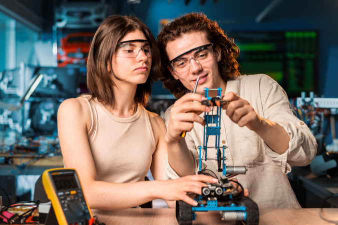 Young man and woman in protective glasses doing experiments in robotics in a laboratory. Robot and tools on the table